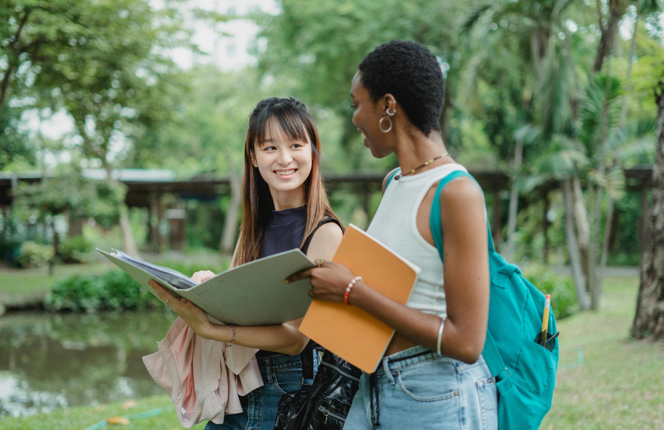 Multiethnic female friends speaking while walking in park with notepads