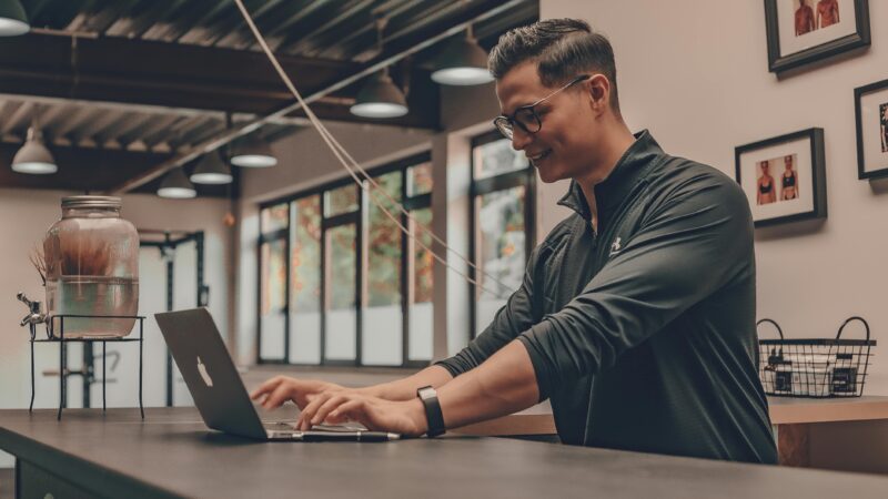 Smiling man working with laptop in gym