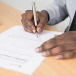 Person Holding Gray Twist Pen and White Printer Paper on Brown Wooden Table